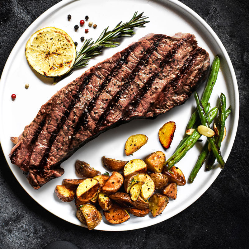 new york strip arranged on a white plate with potatoes and green beans