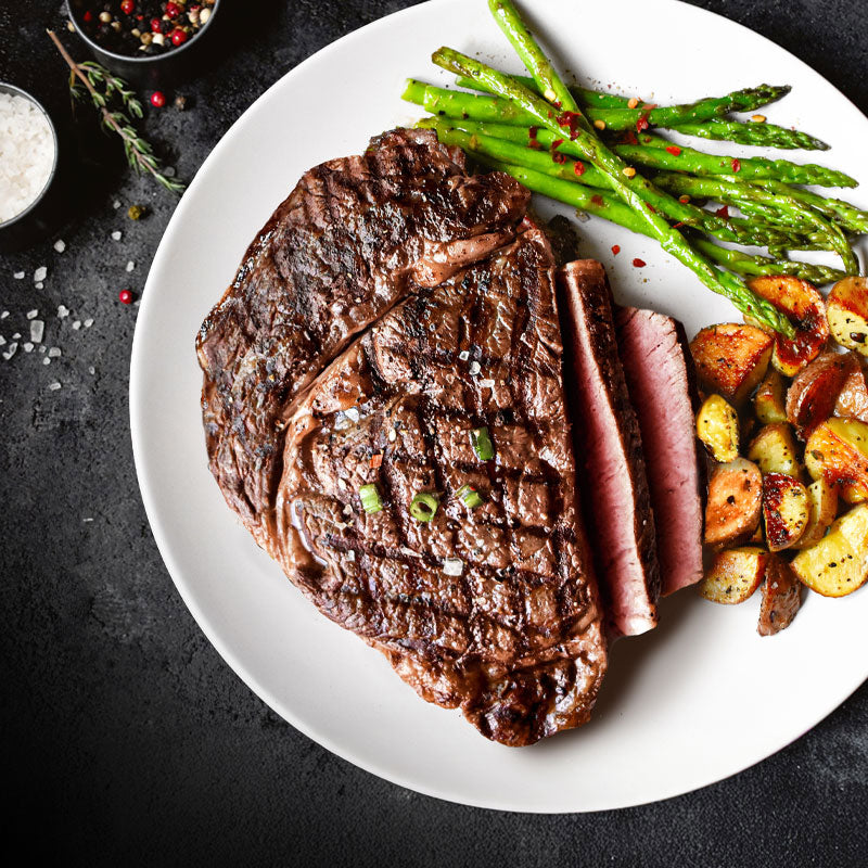 ribeye with potatoes and asparagus on a white plate