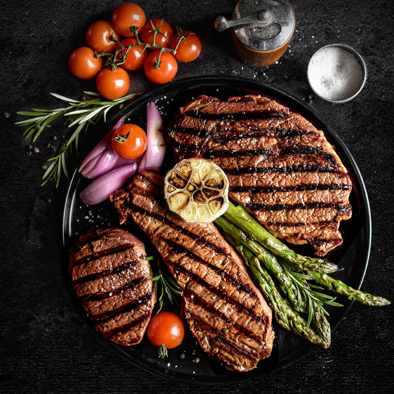 steak lovers triple treat combo on black plate next to vegetables, salt and pepper mill