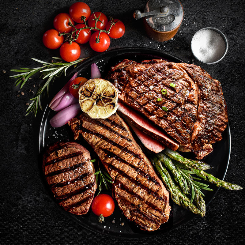 steak lovers triple treat combo on black plate next to vegetables, salt and pepper mill
