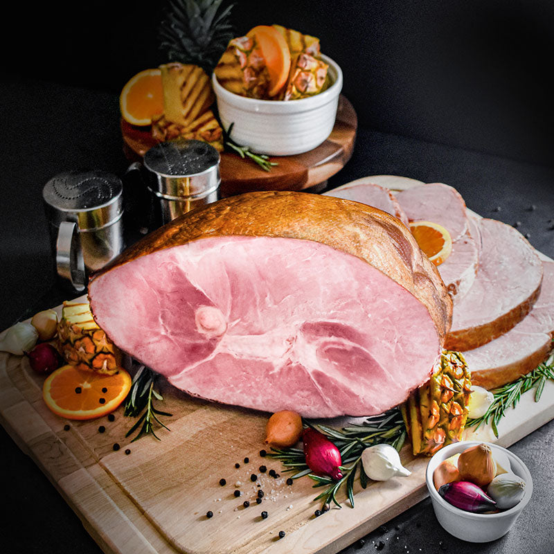 whole bone-in ham partially sliced on a cutting board with pineapple and orange garnish