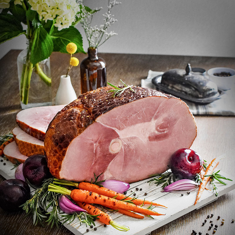 whole bone-in ham sliced on a serving board with plum, shallot, and carrot garnish