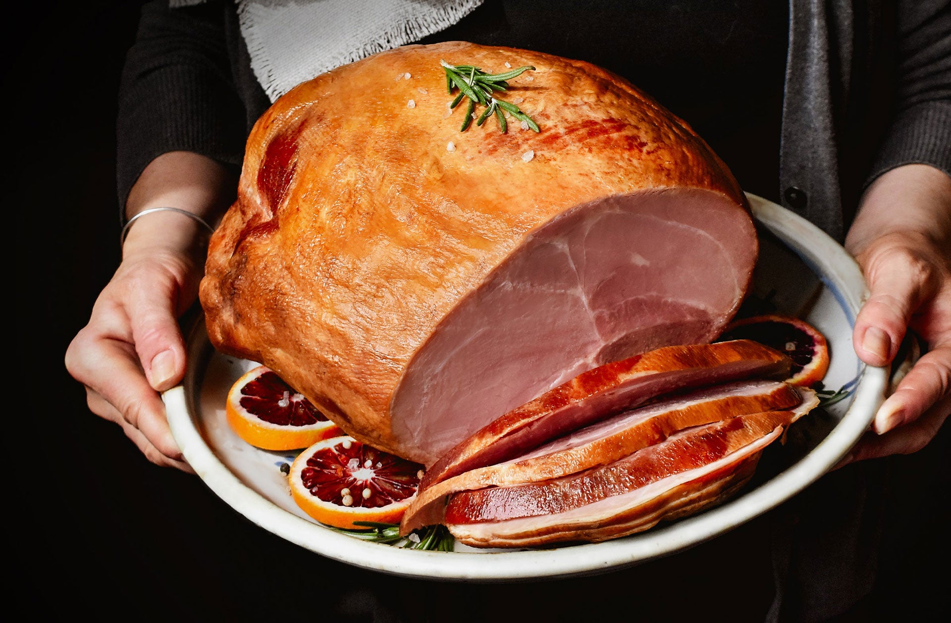 whole bone-in ham sliced on a serving plate held by a person