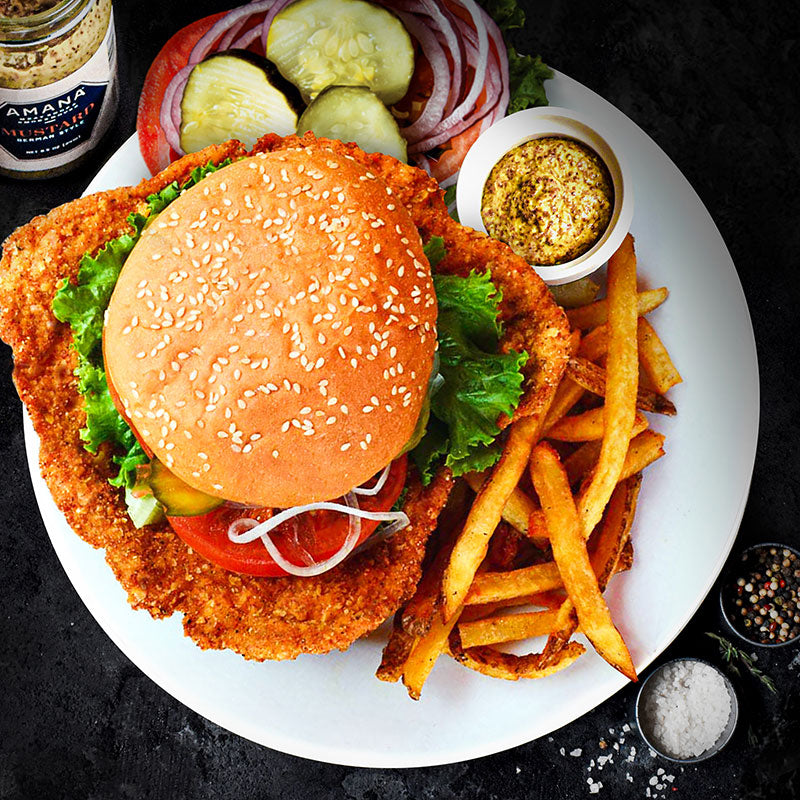 breaded pork tenderloin in a sandwich served with fries on a plate