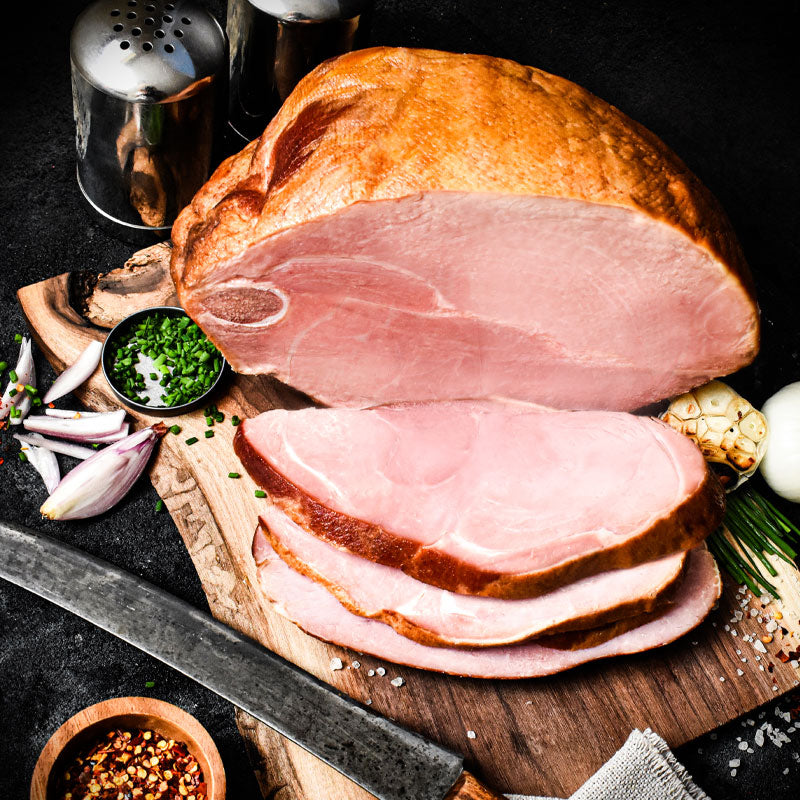 half bone-in smoked ham sliced on a cutting board with garnishes around it