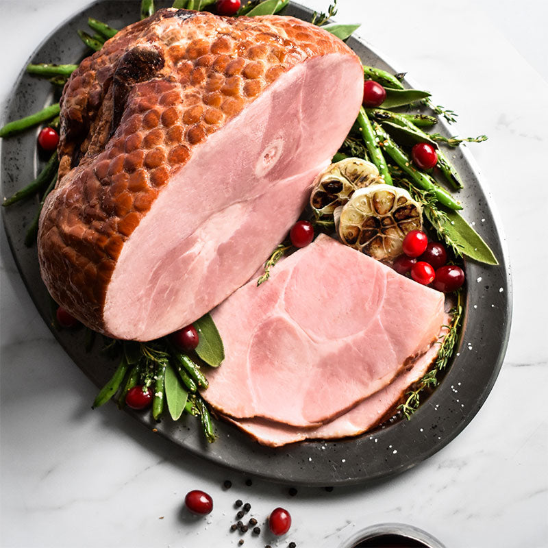 half bone-in smoked ham sliced on a cutting board with garnishes around it