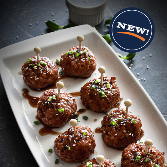 Ham balls on white plate with sauce and scallions, each skewered with a toothpick.