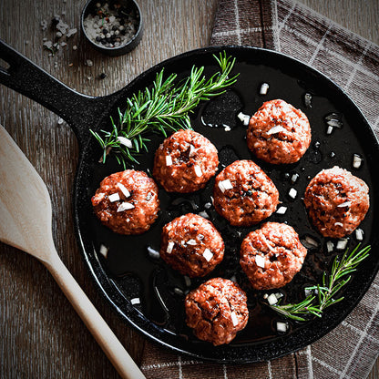 Ham balls being served on a skillet with rosemary garnish and chopped onion.