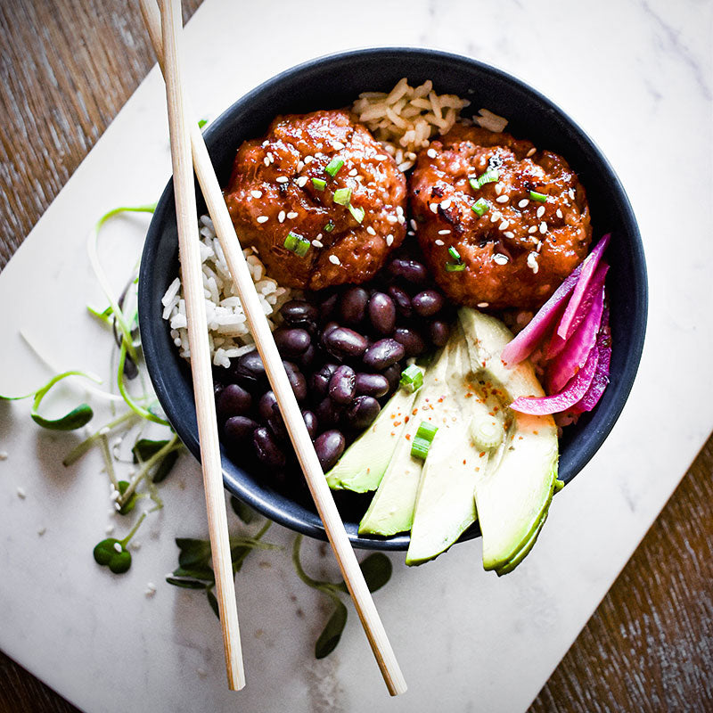 Rice bowl with ham balls, beans, pickled onion, avocado, and chopsticks balanced on edge of bowl.