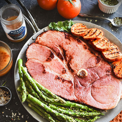 Bone-in ham steak on a tray with grilled sweet potato rounds and asparagus.