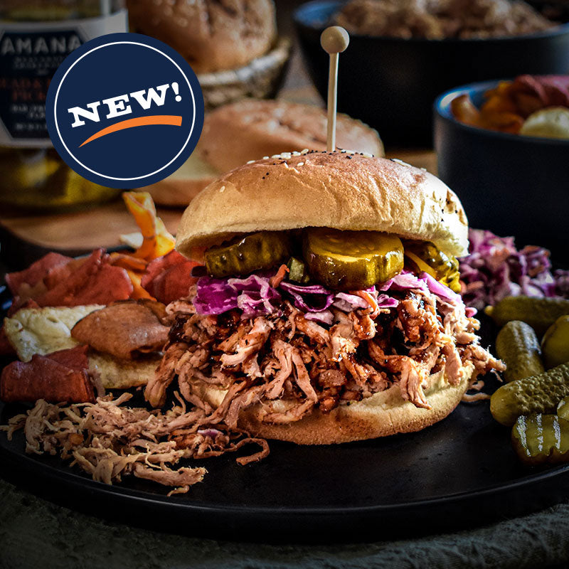 Shredded pork sandwich with pickles and slaw on a black plate.