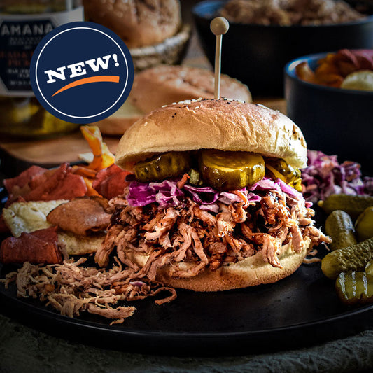 Shredded pork sandwich with pickles and slaw on a black plate.
