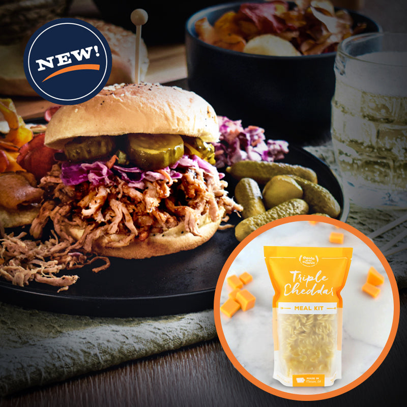 Shredded pork sandwich with pickles and slaw on a black plate. Inset with Pasta of the Prairie Triple Cheddar Meal Kit.