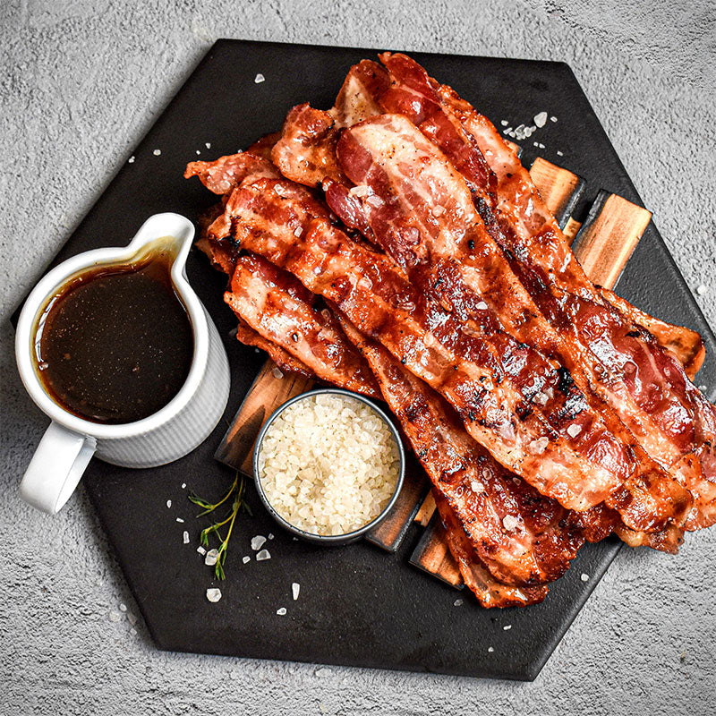 stack of smoked maple bacon next to a cup of maple syrup