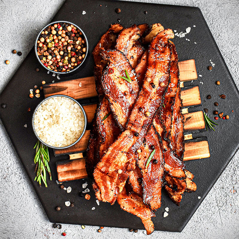 pile of smoked pepper bacon with pepper and salt on a black plate