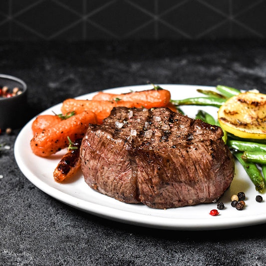 beef tenderloin on a white plate with carrots and green beans