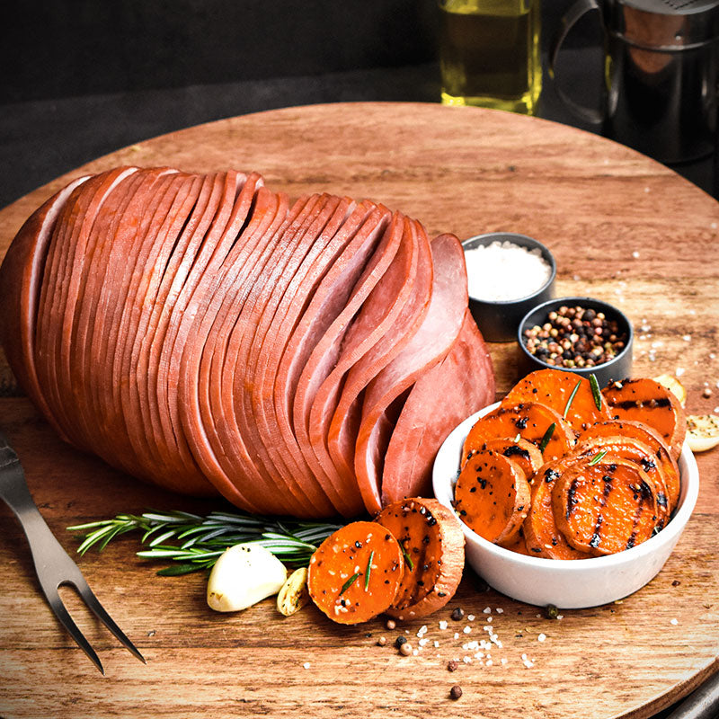 boneless spiral sliced ham on a wooden serving tray with sweet potatoes in front