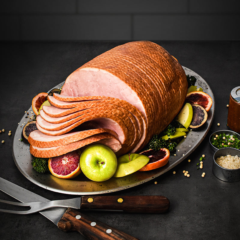 boneless spiral sliced ham on a serving tray with fruit around it