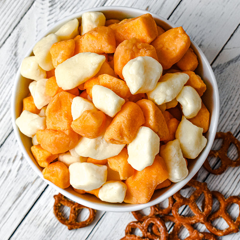 cheese curds in a white bowl with pretzels on a table