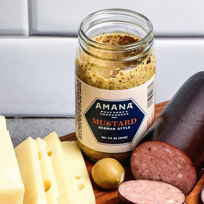 jar of german style mustard surrounded by cheese and meat