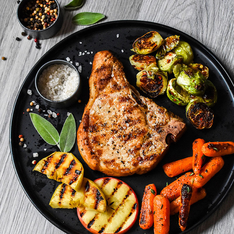 iowa pork chop on a black plate served with vegetables