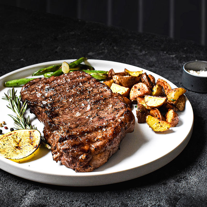 new york strip arranged on a white plate with potatoes and green beans