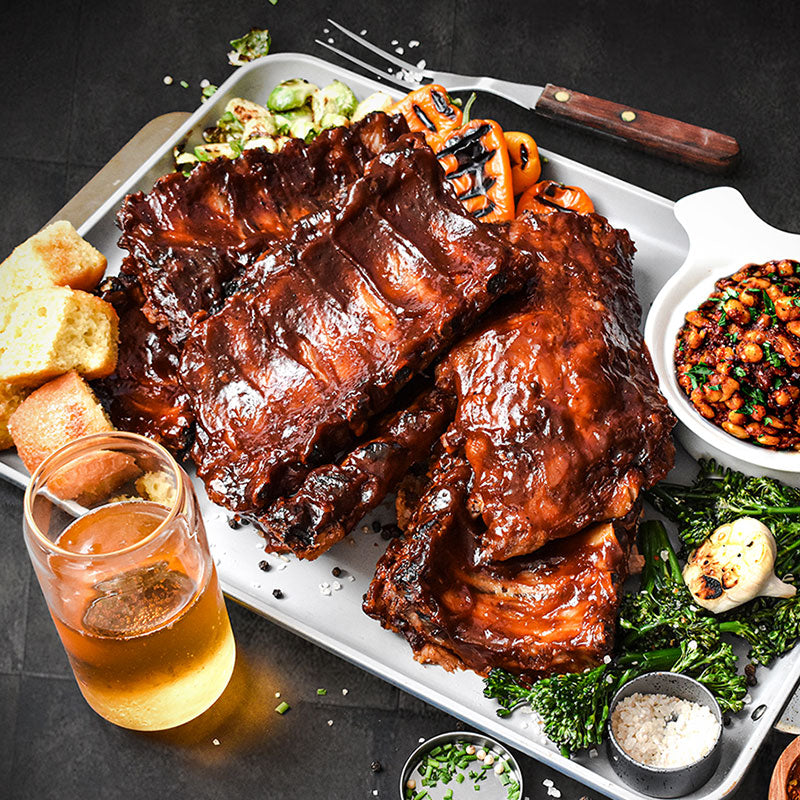 barbeque ribs served with bread beans and drink on a metal platter