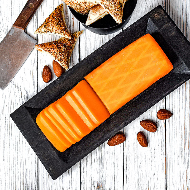 smoked cheddar cheese partially sliced on black cutting block with crackers on the side