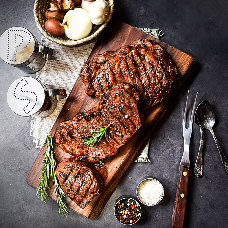 steak lovers triple threat combo on wooden slab next to utensils and salt and pepper