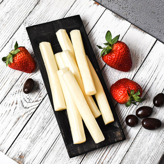 string cheese sticks on a black board with strawberries and chocolate on the side