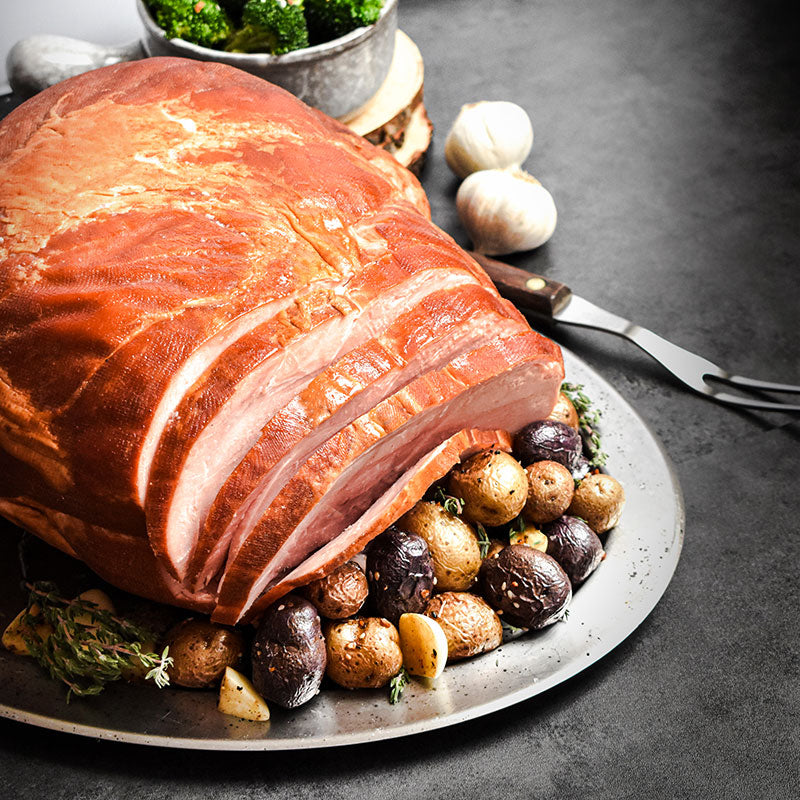 whole bone-in ham partially sliced with potatoes on silver platter