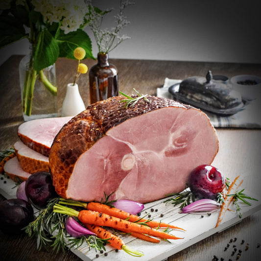 whole bone-in ham sliced on a serving board with plum, shallot, and carrot garnish