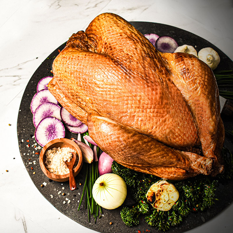 whole turkey served with vegetables around it on black serving platter